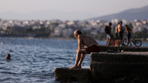Ενας άνδρας κάθεται μόνος του σε προβλήτα παραλίας