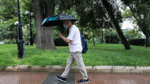 άνδρας με μάσκα και ομπρέλα περπατάει σε δρόμο