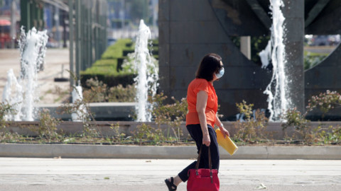 γυναίκα με μάσκα και πορτοκαλί μπλούζα περπατάει 