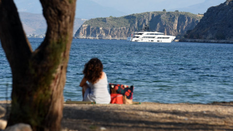 γυναίκα με πορτοκαλί τσάντα κάθεται σε παραλία με άμμο