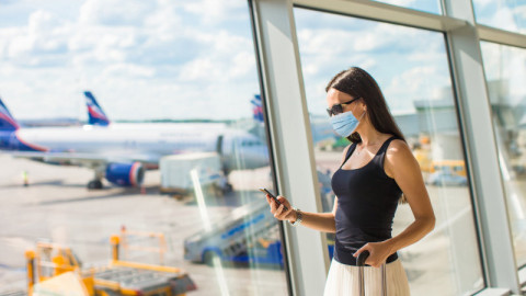 κοπέλα με μάσκα κινητό και βαλίτσα σε αεροδρόμιο για ταξίδι