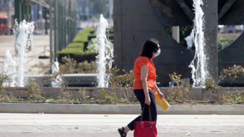 γυναίκα με μάσκα και πορτοκαλί μπλούζα περπατάει
